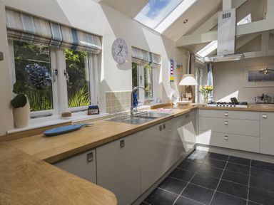 A kitchen with wooden countertops white cabinets a sink a stove and windows with striped blinds at Gooder House in Dartmouth