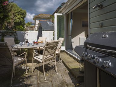 An outdoor patio with a round table and six chairs a barbecue grill and a sliding door to an interior room at Gooder House Dartmouth