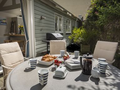 An outdoor patio dining table with coffee, croissants, strawberries, mugs, and plates surrounded by cushioned chairs at Gooder House in Dartmouth