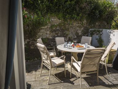 An outdoor patio with a round table set with cups plates and food surrounded by six cushioned chairs at Gooder House in Dartmouth