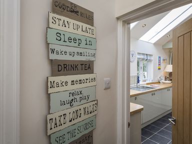 A hallway wall with a decorative sign next to a doorway leading to a kitchen with white cabinets and a skylight at Gooder House in Dartmouth