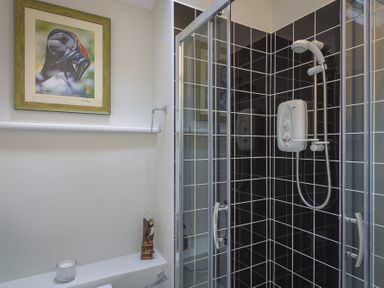 A shower cubicle with black and white tiled walls and a white shower unit in a bathroom at Gooder House in Dartmouth