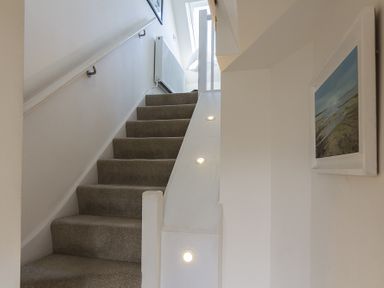 A carpeted staircase with handrail and wall lights leading upstairs with a framed picture on the right wall at Gooder House in Dartmouth