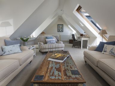 An attic living room with sofas a wooden coffee table a desk and slanted windows at Gooder House in Dartmouth