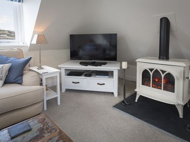 A living room with a beige sofa blue pillows white side table lamp television on white stand and a white stove at Gooder House in Dartmouth