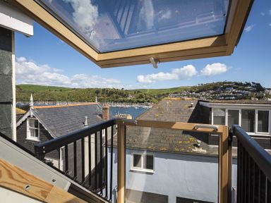 View of rooftops hills and a body of water seen from a balcony with a glass door and black railings at Gooder House in Dartmouth