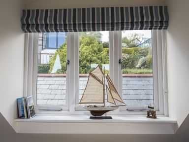 A window with a blue and white striped blind a model sailboat and books on the windowsill at Gooder House in Dartmouth