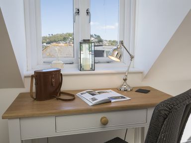 A desk with a brown bag an open book a silver desk lamp and a wicker chair by a window at Gooder House in Dartmouth
