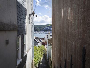 A narrow alleyway between buildings leading to a view of boats on the water and hills in the distance at Gooder House in Dartmouth