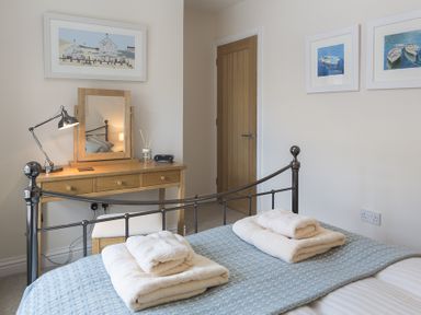 A bedroom with a metal bed frame towels on the bed a wooden dressing table with a mirror lamp and clock at Gooder House in Dartmouth
