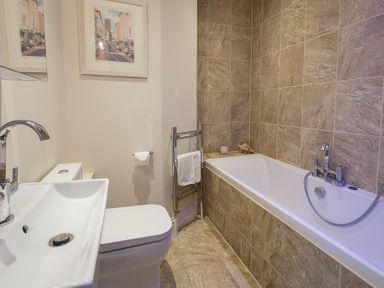 A bathroom with a bathtub, sink, toilet, towel rack, and framed pictures on the wall at Gooder House in Dartmouth