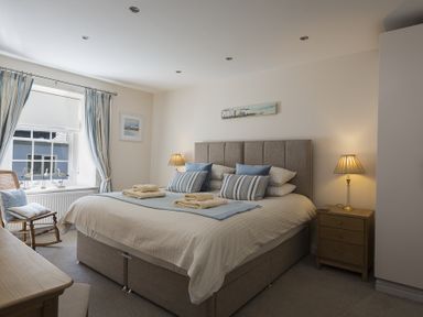 A bedroom with a double bed bedside tables a rocking chair and curtains at Gooder House in Dartmouth