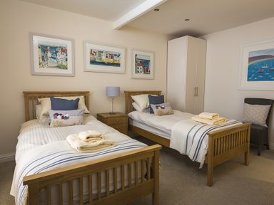 A bedroom with two single beds a nightstand with a lamp a wardrobe a chair and framed pictures on the walls at Gooder House in Dartmouth