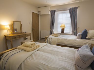 A bedroom with two single beds a wooden dressing table with a mirror a lamp and a window with curtains at Gooder House in Dartmouth