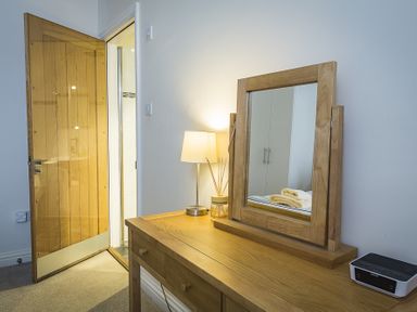 A wooden dressing table with a mirror lamp diffuser and radio near an open wooden door at Gooder House in Dartmouth