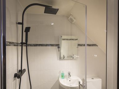 A shower area with a black showerhead and a white sink with a faucet and green soap at Gooder House in Dartmouth