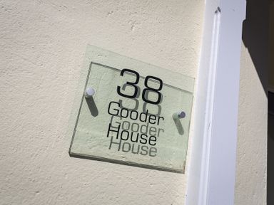 A glass house number sign with the number 38 and the words Gooder House mounted on a cream wall at Gooder House Dartmouth