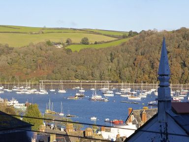 A harbor with many sailboats and a train passing in front of a wooded hillside at Gooder House in Dartmouth