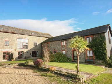 An outdoor view of two stone buildings with small windows surrounded by grass and plants at The Granary Malborough
