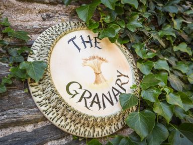 A circular ceramic sign with the words The Granary and a bundle of wheat surrounded by green ivy on a stone wall at The Granary Malborough