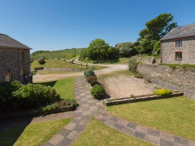 A stone pathway leading to grassy areas and two stone buildings under a clear blue sky at The Granary Malborough