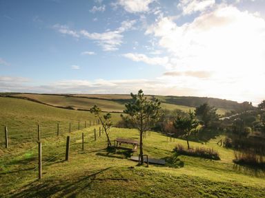 A grassy field with trees a wooden bench and a fence under a blue sky at The Granary Malborough