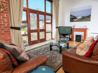 A living room with brown leather sofas a glass coffee table a television and large wooden framed windows at The Granary Malborough