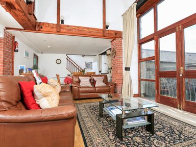 A living room with brown leather sofas a glass coffee table a patterned rug wooden beams and large windows at The Granary Malborough