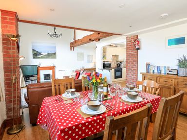 A dining area with a red polka dot tablecloth and set table next to a living room with brown leather sofas at The Granary Malborough