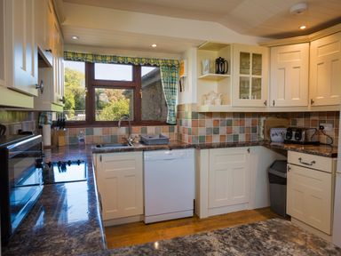 A kitchen with white cabinets a dishwasher a sink and a window with checked curtains at The Granary Malborough