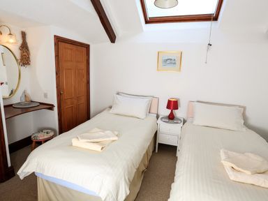 A bedroom with two single beds a nightstand with a lamp a skylight mirror and a wooden door at The Granary Malborough