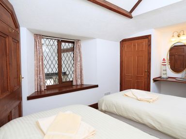 A bedroom with two single beds a window with curtains a wooden door and a vanity area with mirror and lighthouse decoration at The Granary Malborough