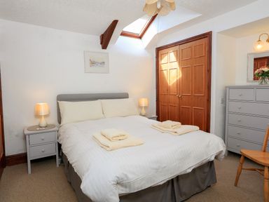 A bedroom with a double bed white bedding bedside tables with lamps wooden doors and a chest of drawers at The Granary Malborough