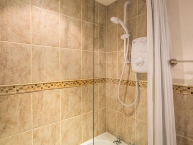 A bathroom shower area with tiled walls a white electric shower unit and a white shower curtain at The Granary Malborough
