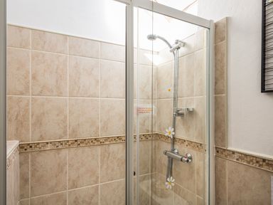 A shower area with beige tiled walls and a glass shower door at The Granary Malborough