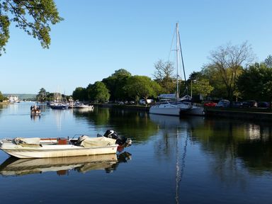 Boats docked on a river with trees and parked cars along the riverbank at The Granary Malborough