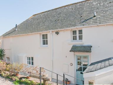 Exterior view of a white cottage with blue door and windows with shutters at Hazel Cottage in Malborough