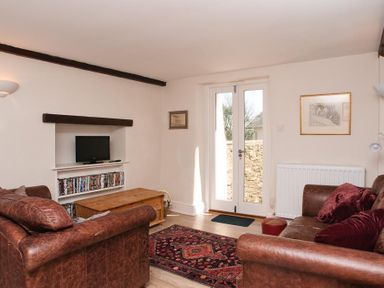 A living room with two brown leather sofas a wooden coffee table a patterned rug and a television on a shelf at Hazel Cottage in Malborough