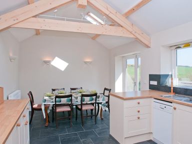 A kitchen with wooden countertops a dining table with chairs and crockery under wooden ceiling beams at Hazel Cottage in Malborough