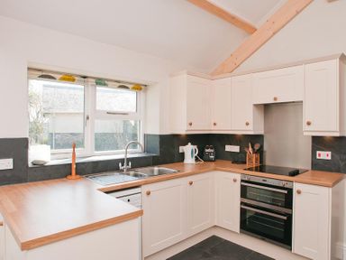 A kitchen with white cabinets wooden countertops a double sink an electric stove a kettle and kitchen utensils at Hazel Cottage in Malborough