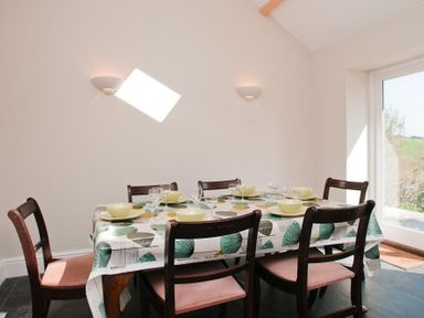 A dining area with a table covered with a patterned tablecloth set with bowls and glasses and six chairs at Hazel Cottage in Malborough
