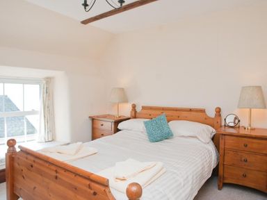 A bedroom with a wooden bed and two bedside tables with lamps at Hazel Cottage in Malborough
