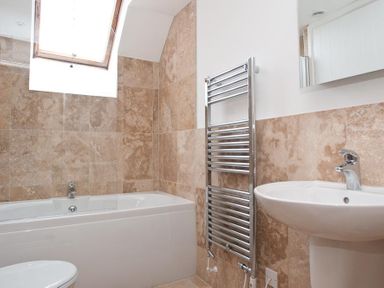 A bathroom with a bathtub toilet sink towel radiator and skylight window at Hazel Cottage in Malborough