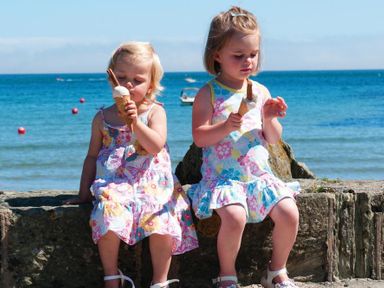 Two young girls sitting on a stone wall by the sea eating ice cream cones at Hazel Cottage in Malborough
