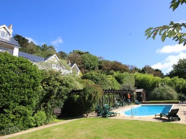 An outdoor swimming pool with lounge chairs and greenery around at The Hoot 16 St Elmo Court in Salcombe