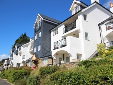 A row of white and grey multi-story residential buildings with balconies and greenery at The Hoot 16 St Elmo Court in Salcombe
