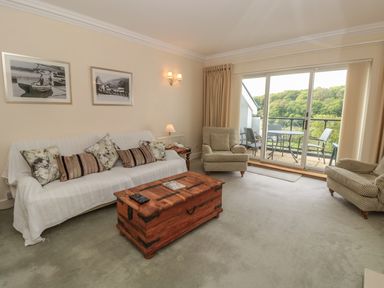 A living room with sofa chairs wooden chest coffee table and sliding glass door leading to balcony at The Hoot 16 St Elmo Court in Salcombe