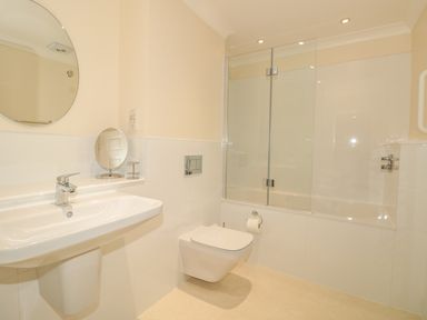 A bathroom with a wall-mounted toilet sink and bathtub with glass shower screen at The Hoot 16 St Elmo Court in Salcombe