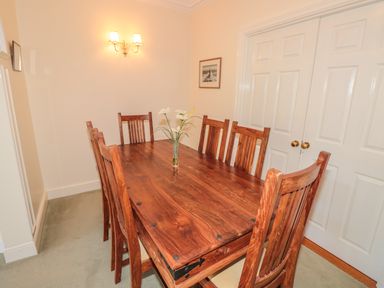 A dining room with a wooden table and chairs and flowers in a vase at The Hoot 16 St Elmo Court in Salcombe