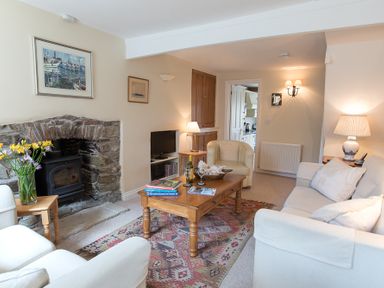 A living room with a stone fireplace a wooden coffee table flowers and cream sofas at Jot Cottage in Salcombe